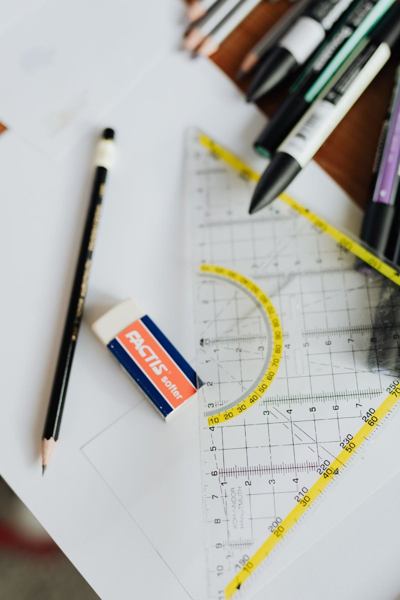 Pencils, markers and a triangle ruler arranged on paper.
