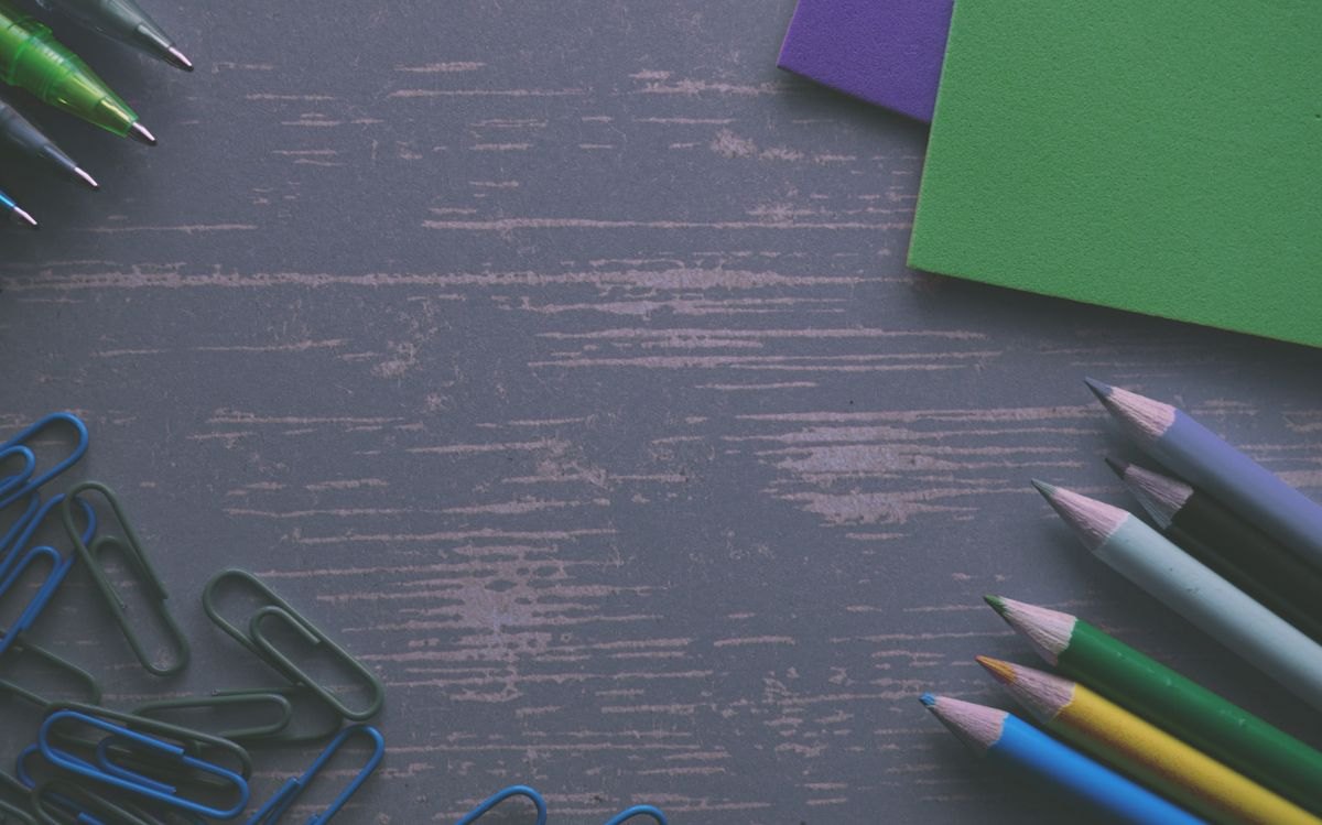 Pencils, paper clips and colored sheets on a wood-textured desk.