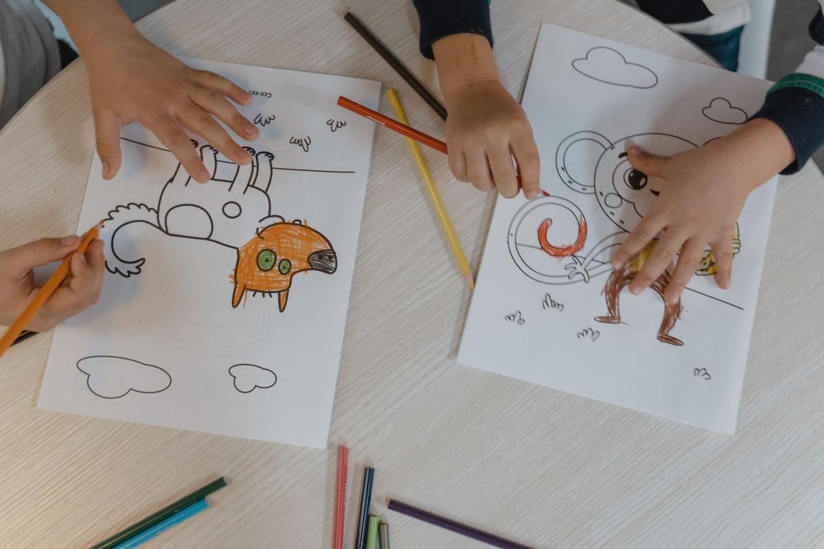 Hands coloring animal drawings on a wooden table.